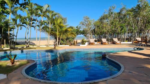 a swimming pool next to a beach with palm trees at pousada mandala in Cumuruxatiba