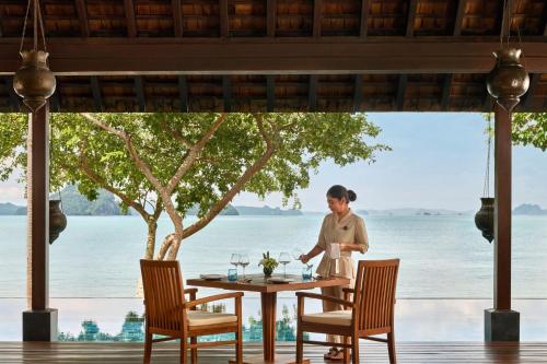 a woman standing at a table in a restaurant with a view of the ocean at Phulay Bay, A Ritz-Carlton Reserve in Tab Kaek Beach