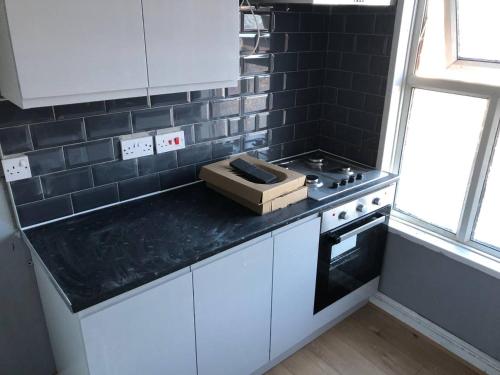 una cocina con armarios blancos y una pared de azulejos negros en Comfy keats place en Bushbury