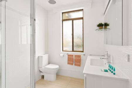 a white bathroom with a toilet and a window at 2-Person Surf Beach Studio App in Surf Beach