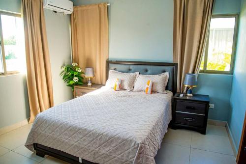 a bedroom with a bed with two lamps and two windows at Beautiful Village 3 bedrooms Furnished Pool residencial Velero punta cana in Punta Cana