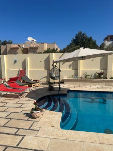 a swimming pool with two chairs and an umbrella at Alis Villa in Hurghada
