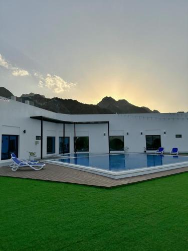 a building with a pool and chairs in the grass at Sheema Lodge in Hatta