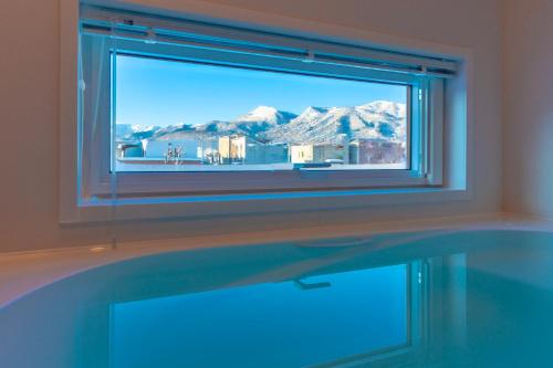 a bathroom with a tub with a window with a view of mountains at FuranoSky - Blue in Furano