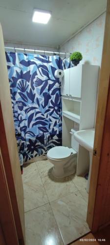 a bathroom with a toilet and a blue and white shower curtain at Casa LLanquihue in Llanquihue