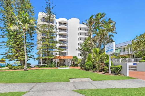 a large white building with palm trees and a park at Albatross North Apartments in Gold Coast