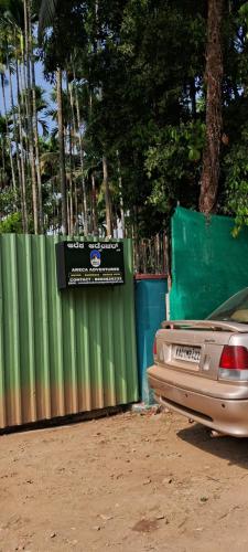 a car parked next to a green fence at Areca Adventures Family Cottage in Kushālnagar