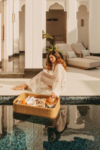 a woman sitting on the floor next to a basket in the water at Raffles Al Areen Palace Bahrain in Manama