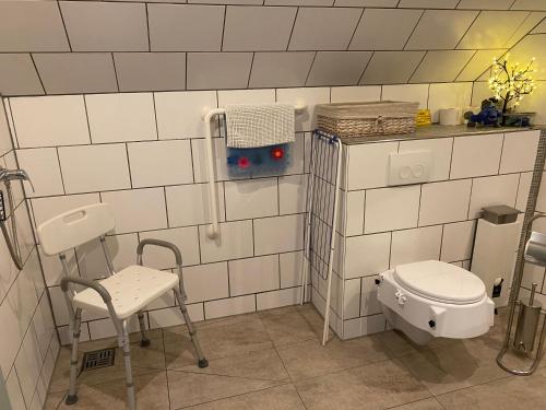 een wit betegelde badkamer met een toilet en een stoel bij Ferienwohnung Gartenblick in Nordenham