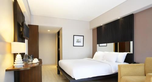 a bedroom with a white bed and a chair at Hotel Santika Kuta in Kuta
