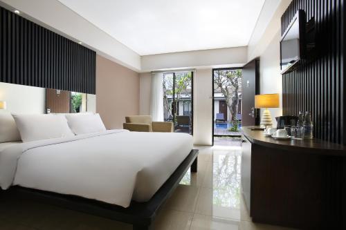 a bedroom with a large white bed and a television at Hotel Santika Kuta in Kuta