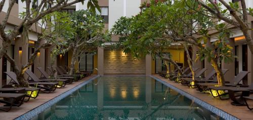 a swimming pool with chairs and trees next to a building at Hotel Santika Kuta in Kuta