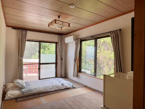 a bedroom with a bed and two windows at ビーチサイドペンションみーばる in Nanjo