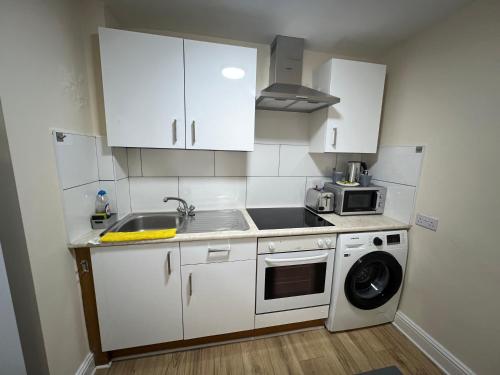 a kitchen with white cabinets and a sink and a washing machine at Station Lodge in London