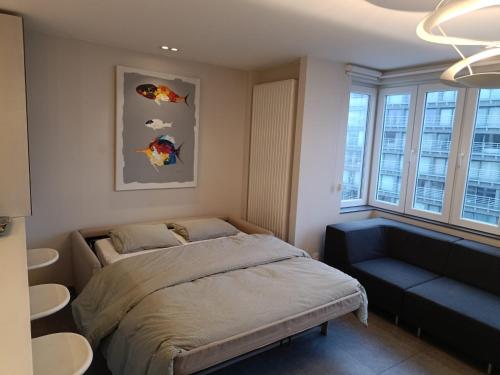 a bedroom with a bed and a couch and windows at Modern appartement - Zeezicht - Perfecte ligging in Koksijde