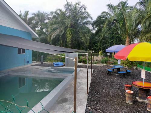 a pool with an umbrella and picnic tables next to a house at AA Burger Homestay for Musliim Only in Banting