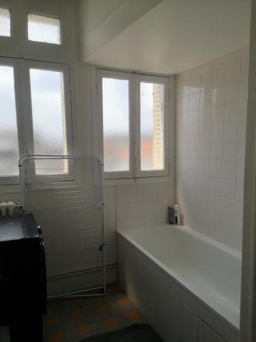 - une salle de bains blanche avec baignoire et 2 fenêtres dans l'établissement Maud’s apppartment, à Asnières-sur-Seine