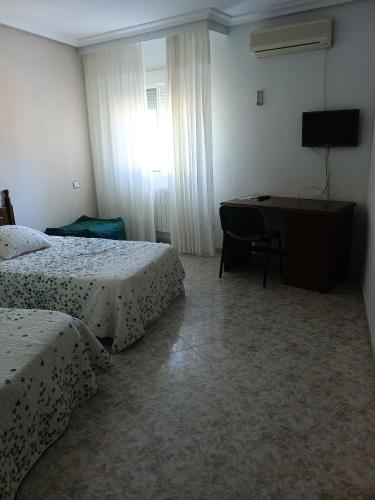 a bedroom with two beds and a desk with a television at EL ABAD in Abadía