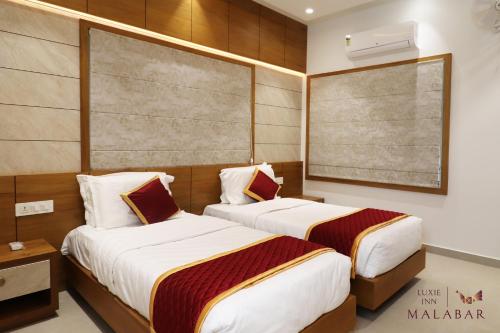 two beds in a hotel room with a large window at LUXIE INN MALABAR in Perintalmanna