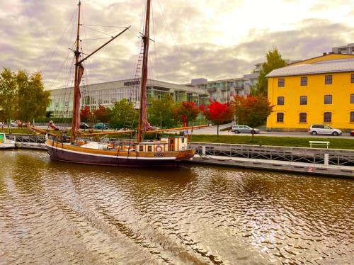 a sail boat docked in a river next to a yellow building at Riverside Loft With Sauna in Turku