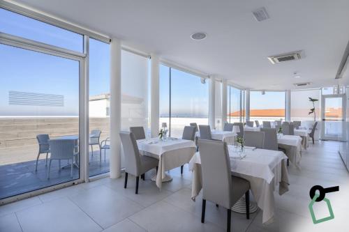 a restaurant with white tables and chairs and large windows at HOTIDAY Room Collection - Tirrenia in Tirrenia