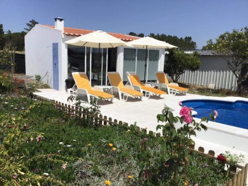 a pool with chairs and umbrellas next to a house at Monte da Palmeirinha in Vila Nova de Milfontes