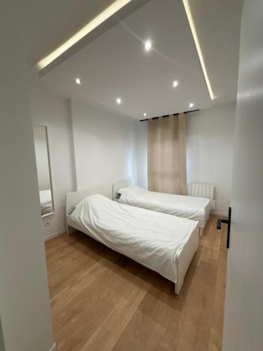 Appartement moderne في فيليوربان: سريرين في غرفة بجدران بيضاء وأرضية خشبية