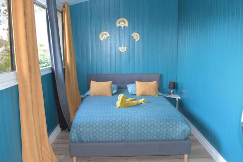 une chambre bleue avec un lit avec un animal rembourré jaune dans l'établissement les pieds dans l'eau 4 personnes, à Cilaos