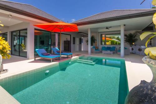 uma piscina com um guarda-sol vermelho e cadeiras e uma casa em Villa Tropical Cocoon em Koh Samui 