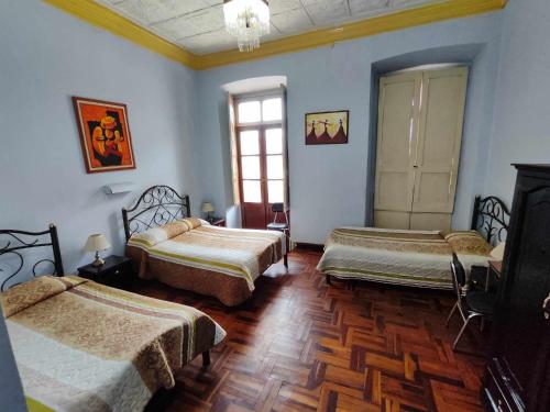 drie bedden in een kamer met blauwe muren en houten vloeren bij Hostal Juana de Arco in Quito