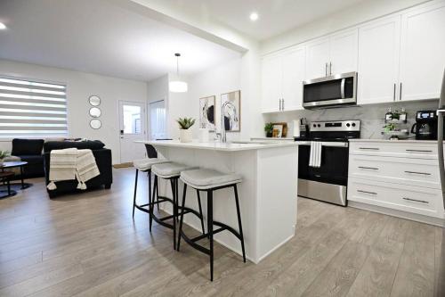 a kitchen with white cabinets and bar stools at Escape in Style, Golf,King Beds,Disney+,Near WEM in Edmonton