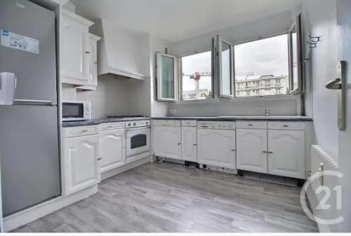 una cucina con elettrodomestici bianchi e 2 finestre di Très charmant appartement proche de Paris ad Aulnay-sous-Bois