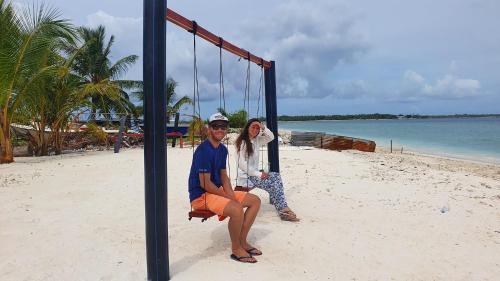a man and woman sitting on a swing on the beach at Finimas Residence in Thimarafushi