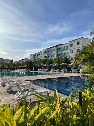 um resort com uma piscina com cadeiras e guarda-sóis em Palm Village Família Flats 03 Qrts em Ipojuca