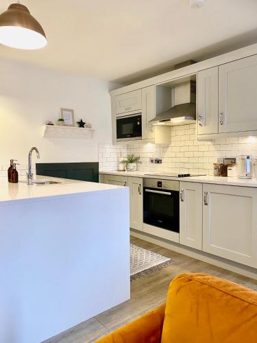 a kitchen with white cabinets and an orange couch at Boutique Chapel Apartment within City Walls in Chester
