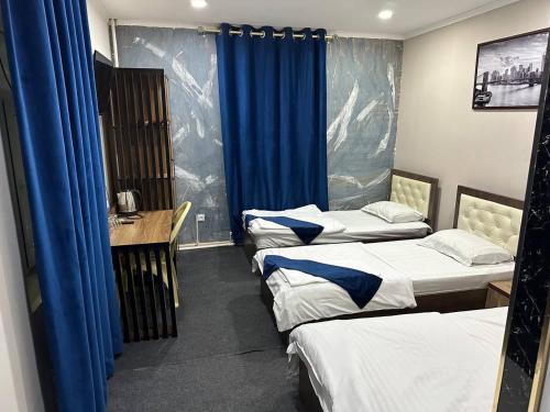 a room with three beds and a table and blue curtains at Ilhombek Guest House Hotel in Tashkent