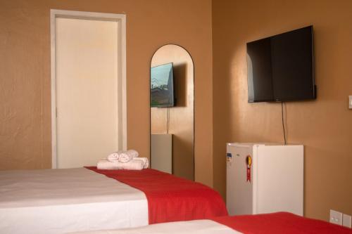 a room with two beds and a refrigerator with a flat screen tv at Porteño Loft Búzios in Búzios