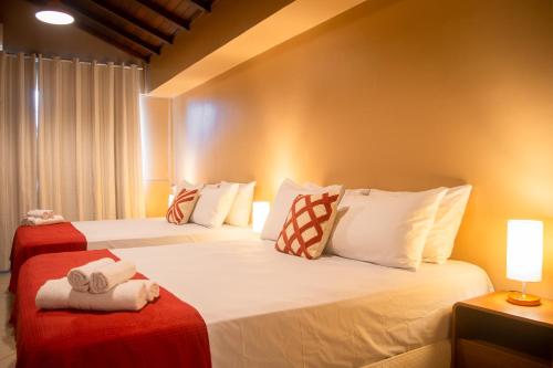two beds in a hotel room with white and red sheets at Porteño Loft Búzios in Búzios