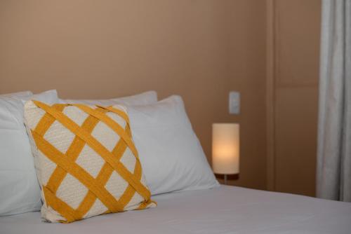 a bed with a yellow and white pillow and a lamp at Porteño Loft Búzios in Búzios