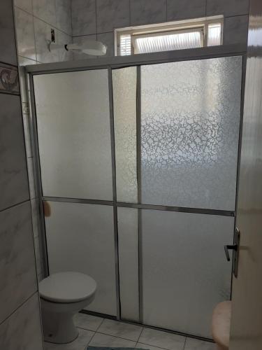 een badkamer met een toilet en een glazen douchedeur bij Casa com boas acomodações in Itanhaém