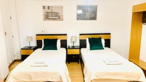 2 letti in una camera con lenzuola bianche e cuscini verdi di Invicta Porto Guest House a Porto
