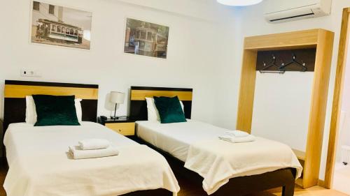 2 letti in una camera con lenzuola bianche e cuscini verdi di Invicta Porto Guest House a Porto