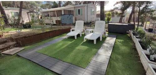 une cour avec deux chaises, une table et de la pelouse dans l'établissement Mobil home Oasis Village 5*, à Puget-sur Argens