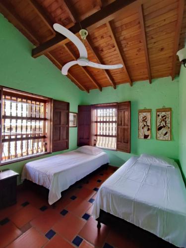 2 camas en una habitación con paredes y ventanas verdes en Hostal La Pola, en Santa Fe de Antioquia
