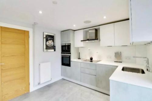 a white kitchen with white cabinets and a sink at Recently renovated,modern house. train station in North Mimms