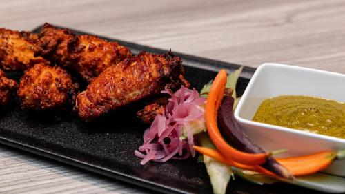 a black plate with chicken wings and a bowl of sauce at Kimpton Hotel Palomar Los Angeles Beverly Hills by IHG in Los Angeles