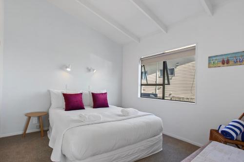 a white bedroom with a bed with purple pillows at Beverley Hills Guesthouse in Whangamata