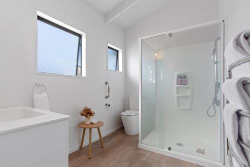 a white bathroom with a shower and a sink at Beverley Hills Guesthouse in Whangamata
