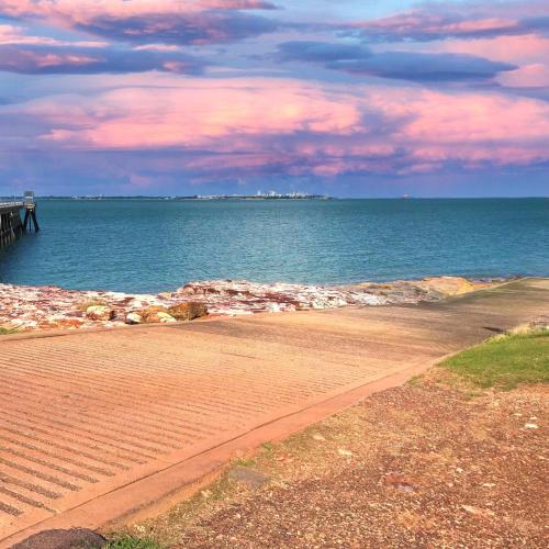 a beach with a pier and the ocean with clouds at Unit 1 Golden Sands Retreat in Wagait Beach