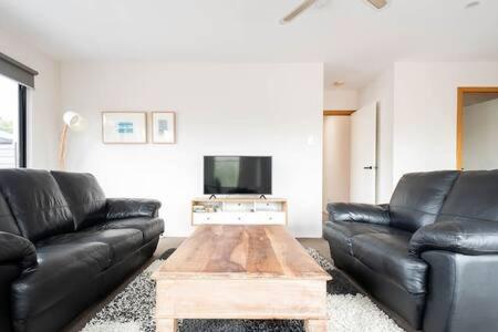 a living room with two black leather couches and a coffee table at CBD Apartment with WiFi & Parking in Launceston